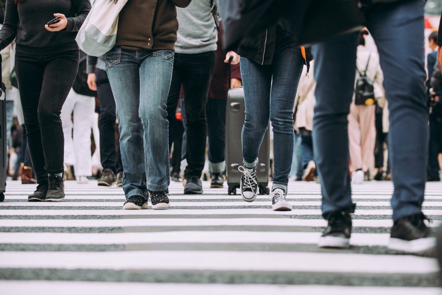 Low-angle view of a dense crowd of people crossing a wide zebra-striped intersection in Tokyo.