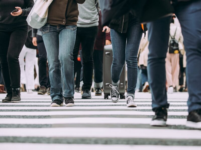 Low-angle view of a dense crowd of people crossing a wide zebra-striped intersection in Tokyo.