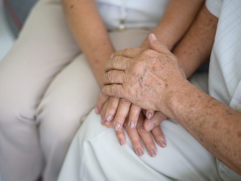 Close-up of younger hands gently holding the aged wrinkled hands of an elderly person.